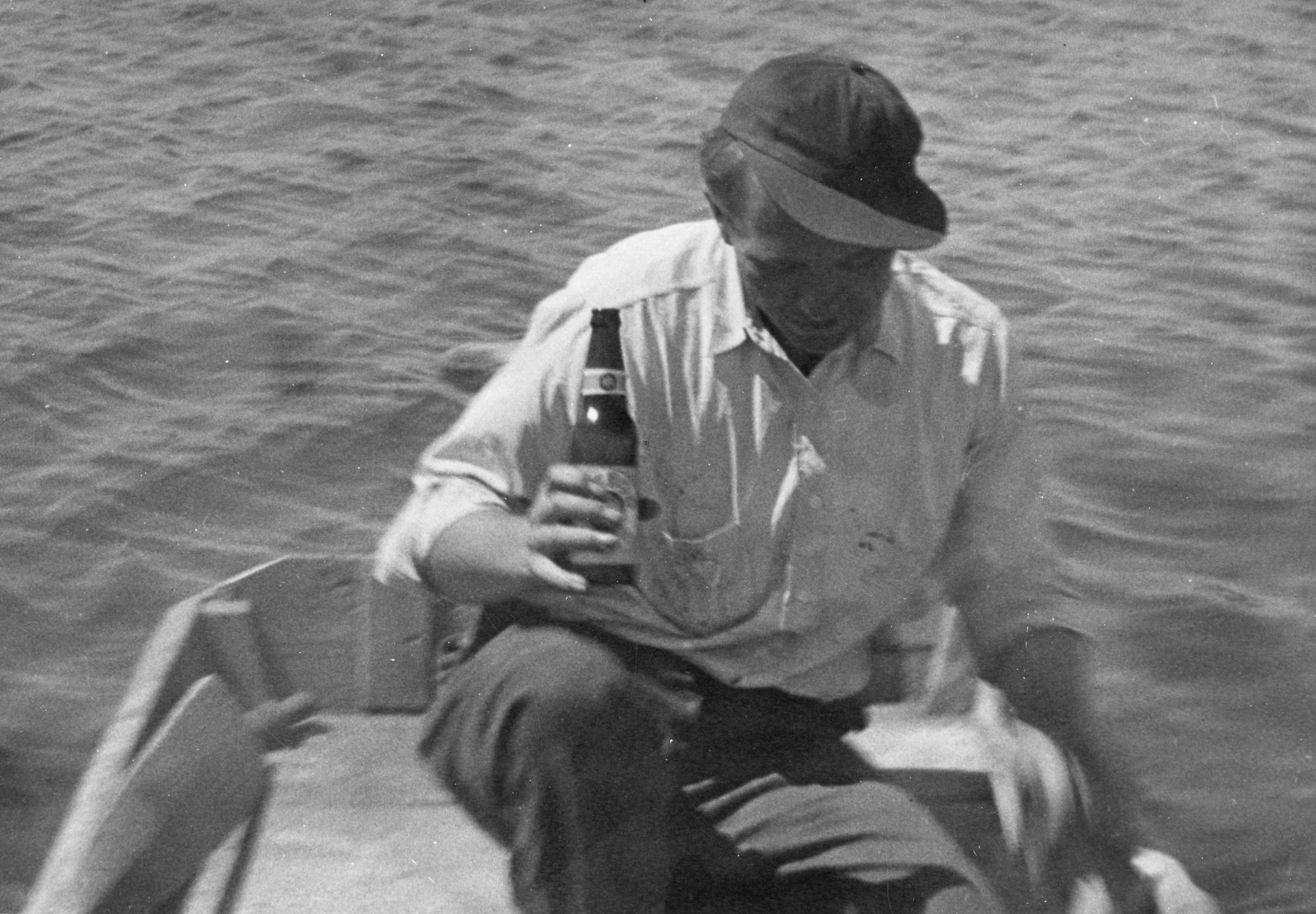 An unknown person sitting in a boat while holding a bottle of beer.