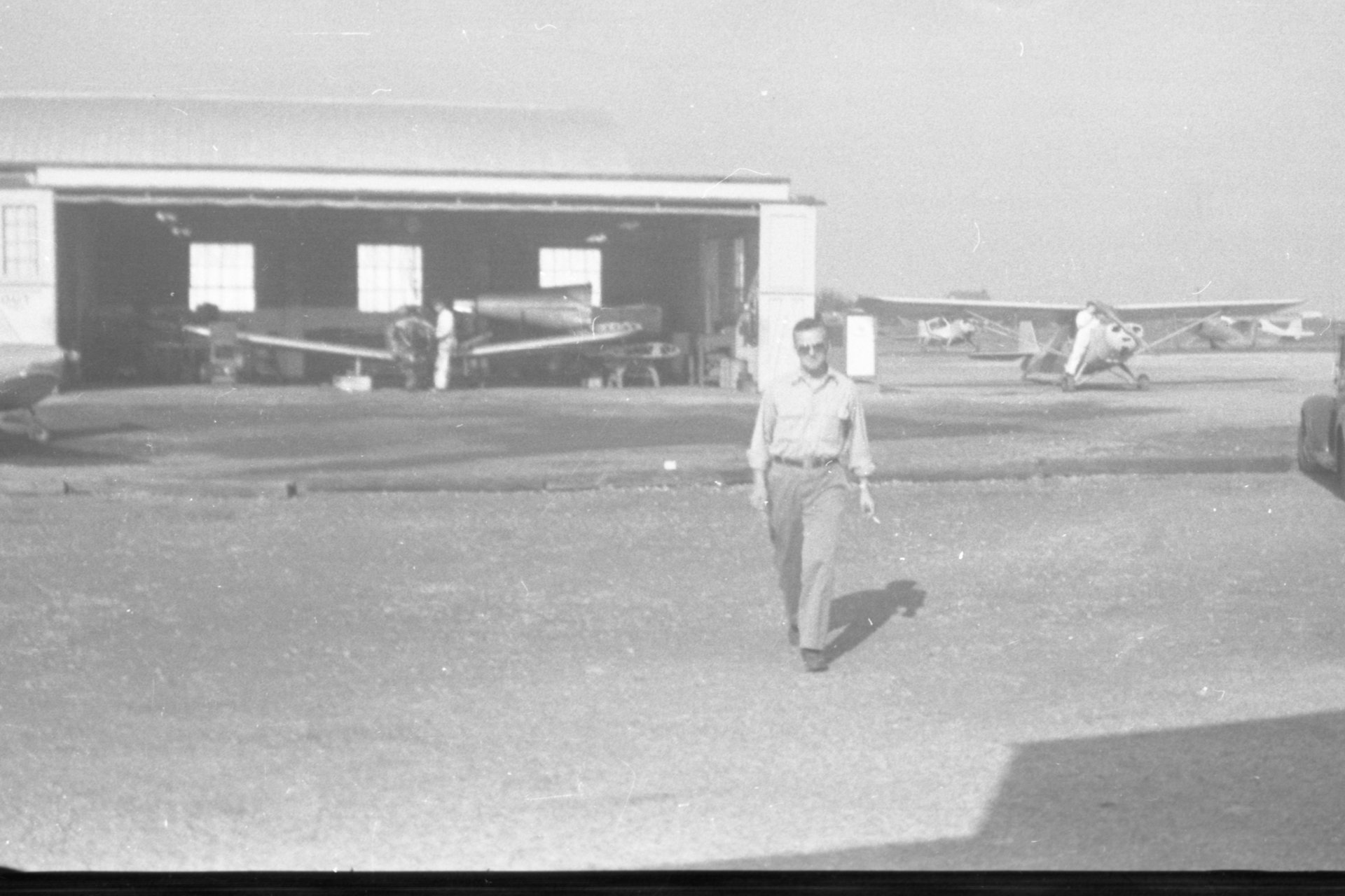 An unknown person walking towards the camera at Buffalo Airpark with the Maintenance shop in the background.