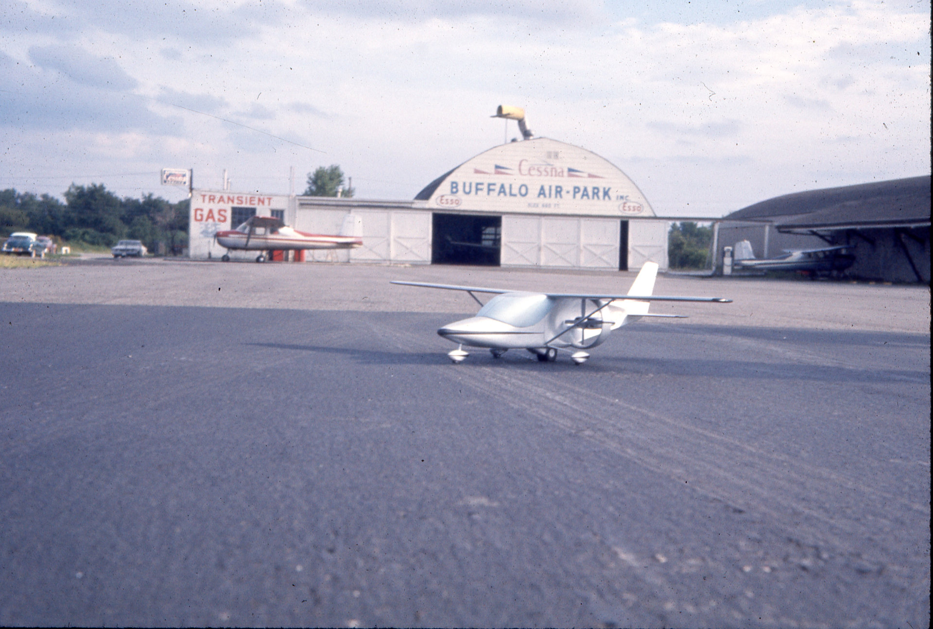 Tony Riccio's model airplane sitting on the tarmac at Buffalo Airpark with the Quonset hangar in the background.