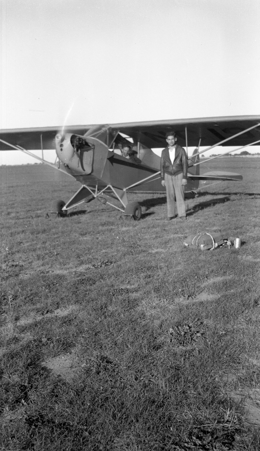 Tony Riccio standing next to a running Tayler "Cub" J-2 with a parachute pack on the ground.