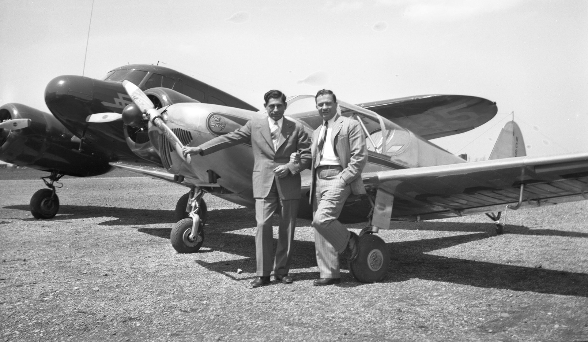 Tony Riccio and an unknown person standing next to a Globe Swift airplane with a Cessna T-50 plane in the background.