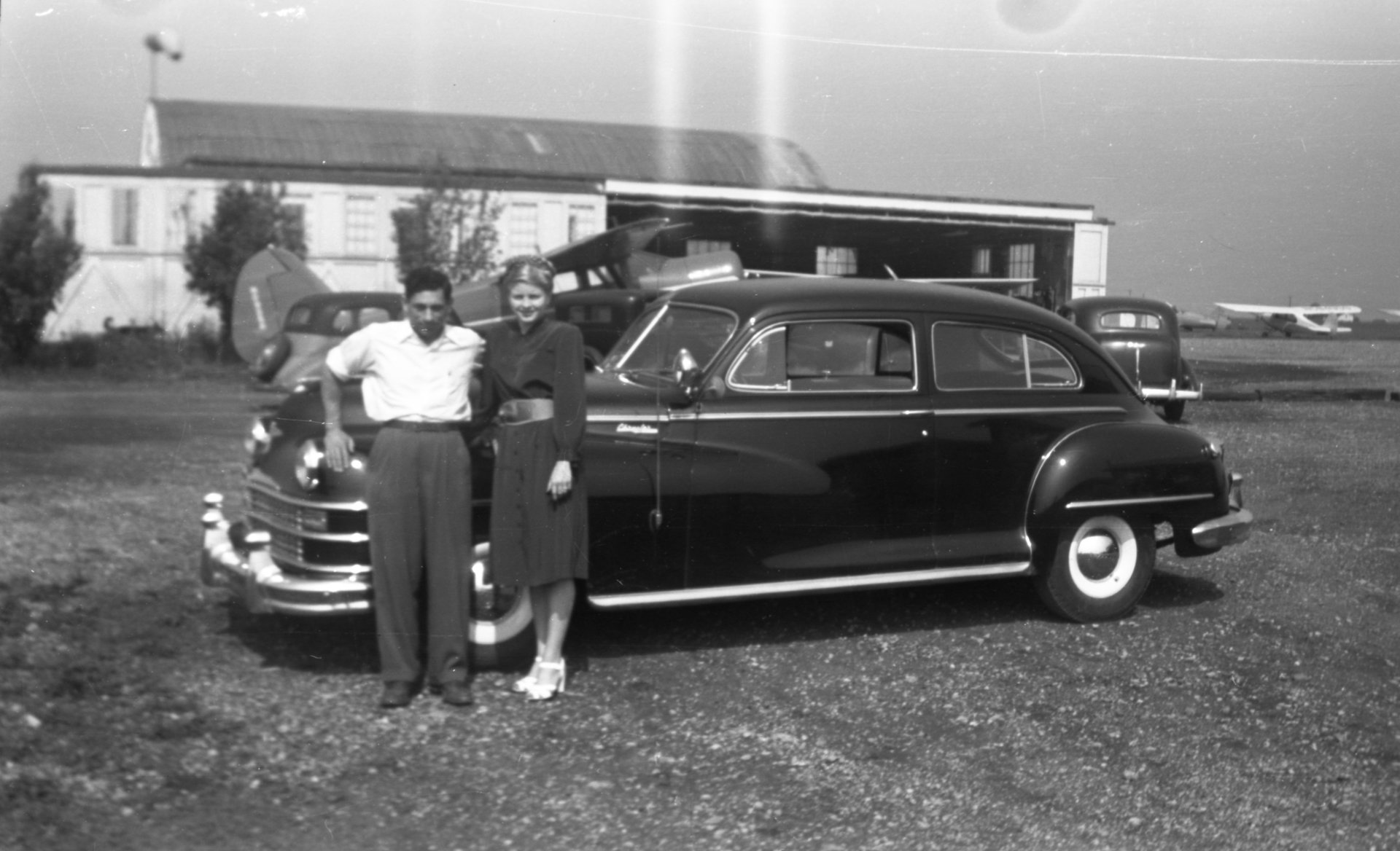 Tony Riccio and his wife Maxine standing in front a car with the Buffalo Airpark's maintenance shop in the background.