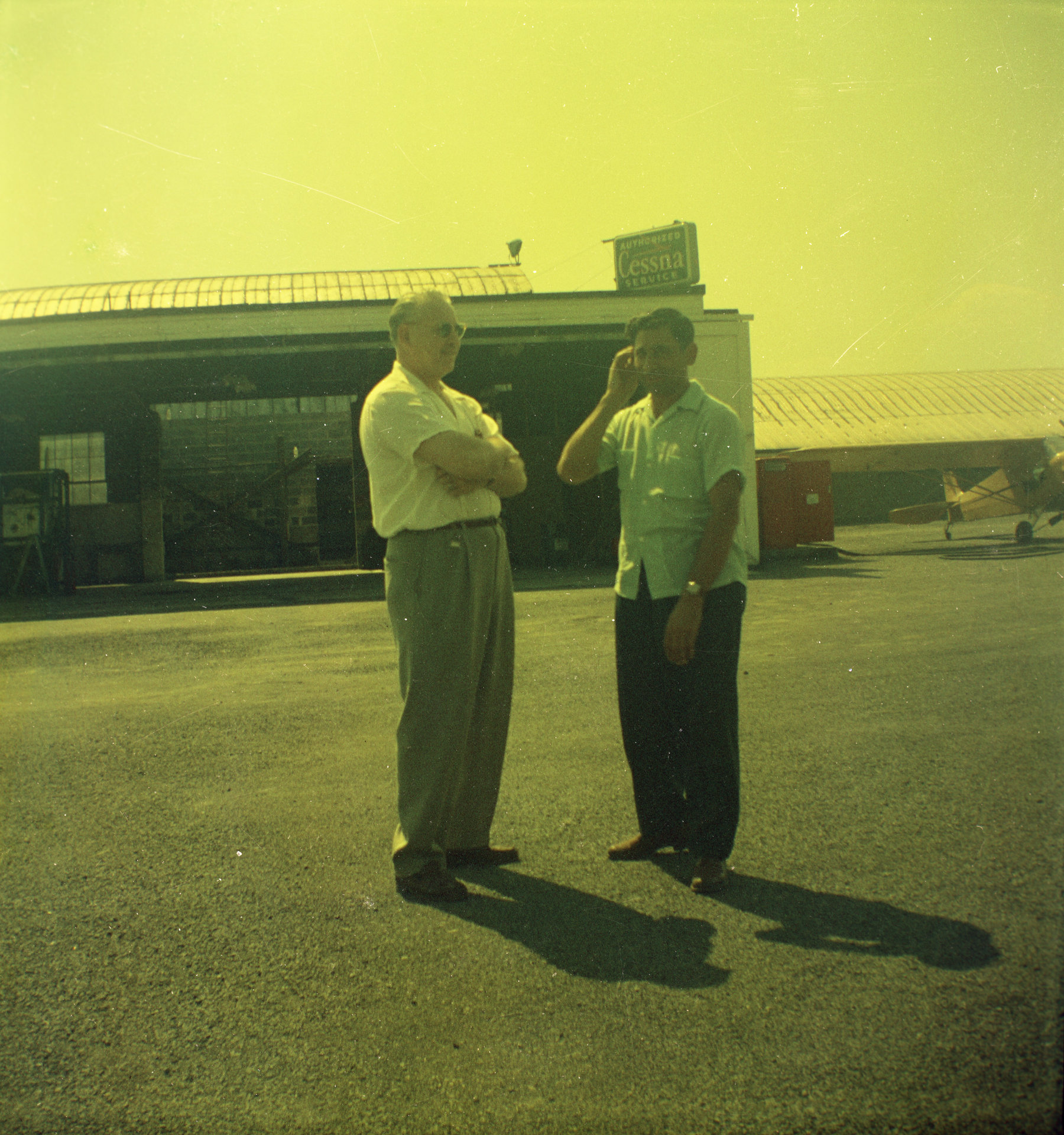 Tony Riccio and an unknown person standing on the tarmac at Buffalo Airpark with the maintenance shop in the background.