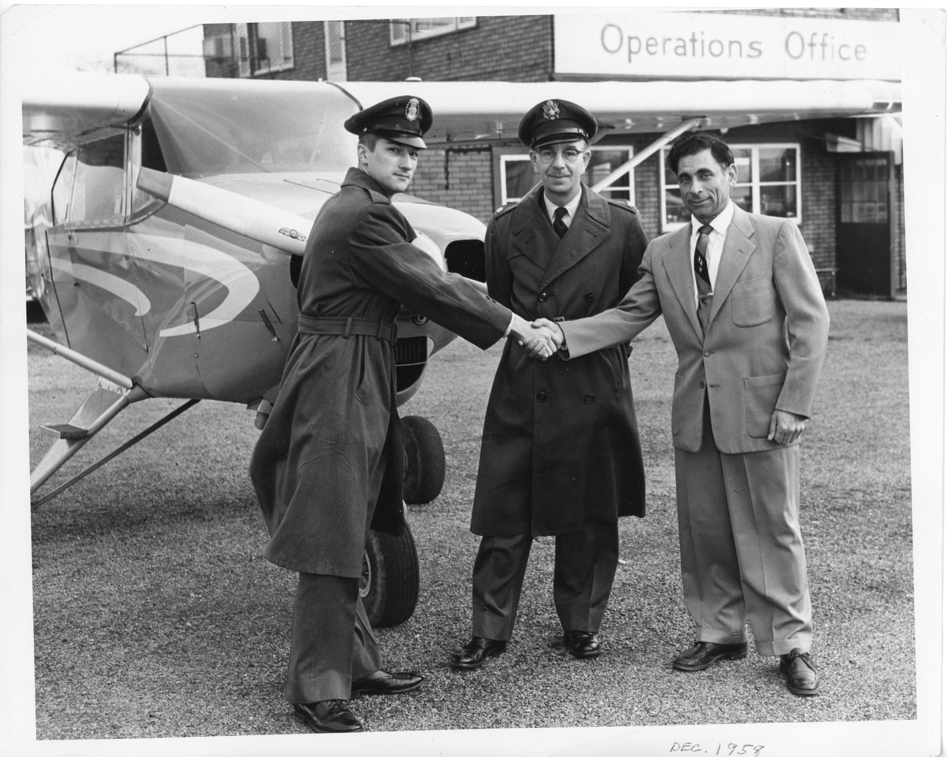 Tony Riccio and two unknown people shaking hands in front of an airplane at Buffalo Airpark in December 1958.
