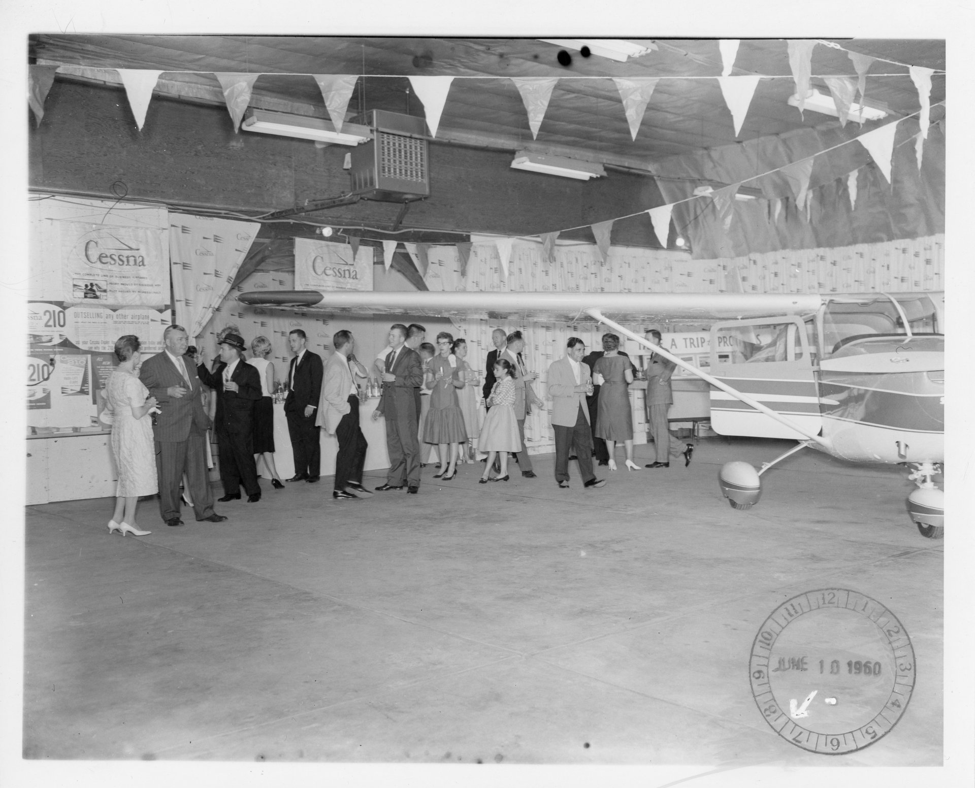Tony Riccio and a group of unknown people gathered in the Buffalo Airpark's Quonset hangar for a Cessna marketing event on June 10, 1960.